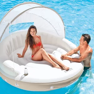 Young Woman Laying In Inflatable Floating Lounge Island With A Canopy For Shade Next To Young Guy